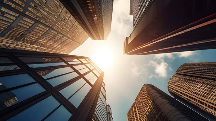 A view from the ground looking up at towering skyscrapers against a clear blue sky in an urban cityscape.