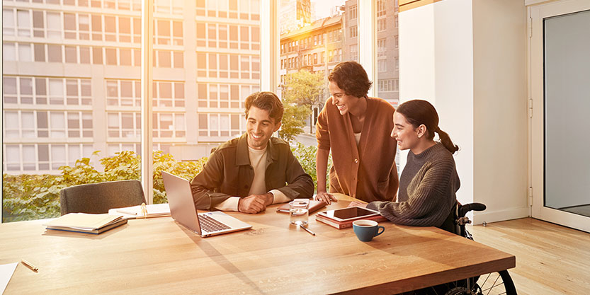 Three office workers gathered around desk working together with urban scenery behind them