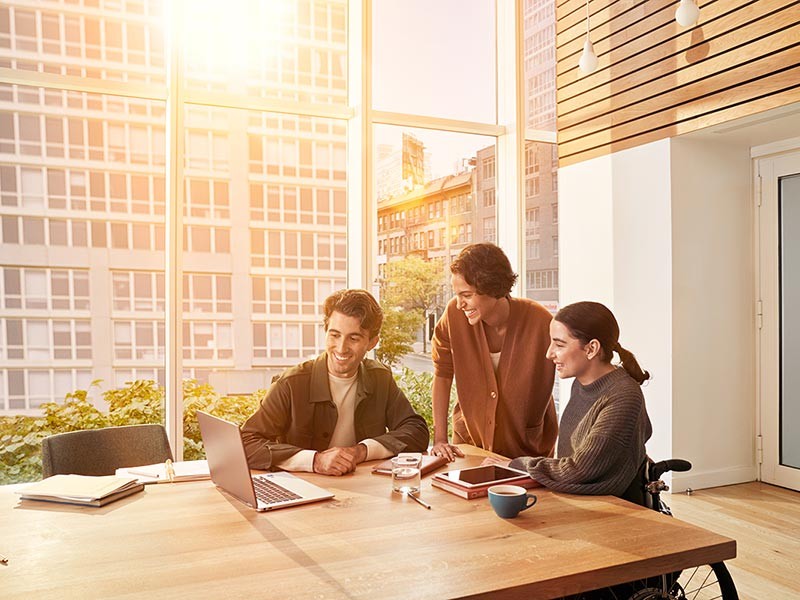 Three office workers gathered around desk working together with urban scenery behind them