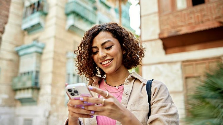 Young woman surrounded by buildings looking at smart phone to access directions and information in a historic city.