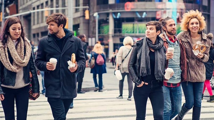 A group of five people, wearing winter clothes, walk across a city street.