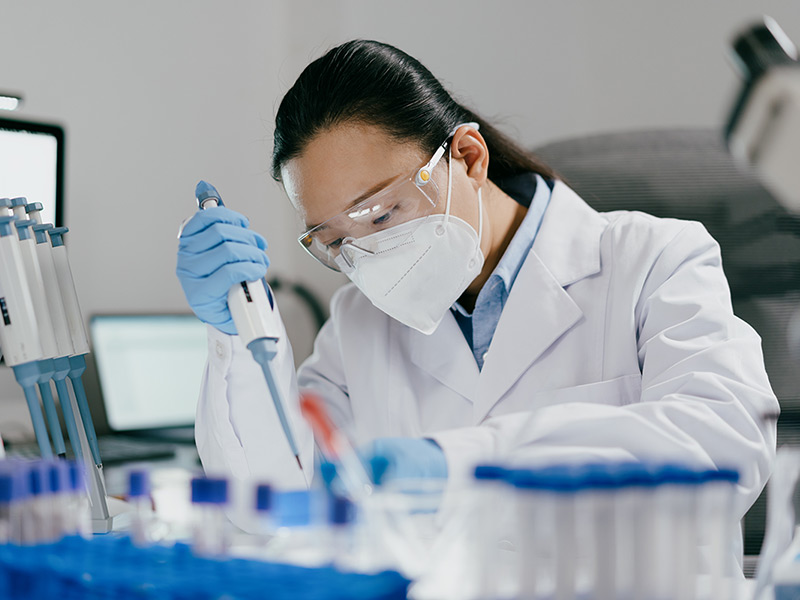 A female scientist in a lab coat and mask conducts an experiment with a test tube in a laboratory environment.