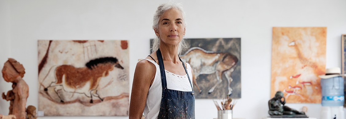 Female artist holding a paint brush standing in front of paintings