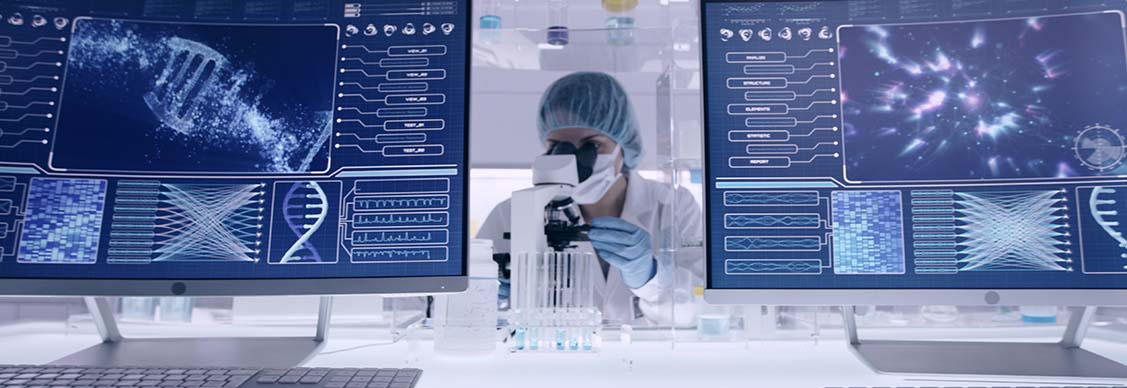 Life sciences laboratory with a scientist at work between two computer screens showing scientific data.