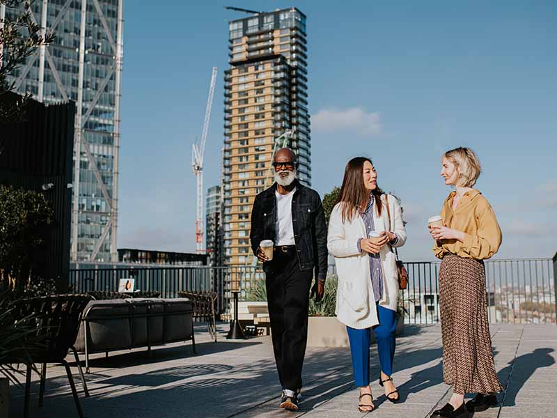 Three people in smart-casual business attire walk together on a roof top