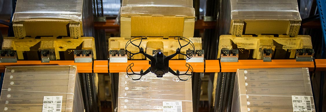 A drone navigates through a warehouse, capturing images of stacked boxes in an organized setting.