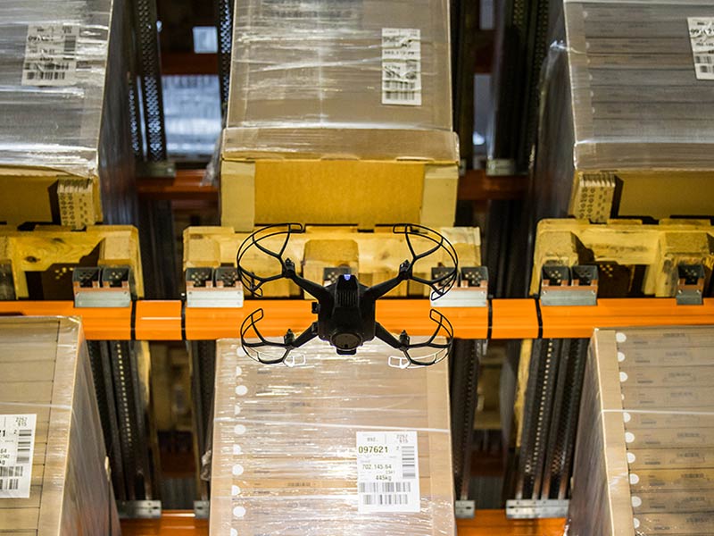 A drone navigates through a warehouse, capturing images of stacked boxes in an organized setting.