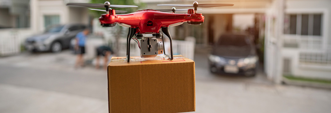 A red drone is seen flying over a house, transporting a box, illustrating modern delivery technology.