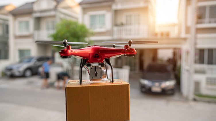 A red drone is seen flying over a house, transporting a box, illustrating modern delivery technology.