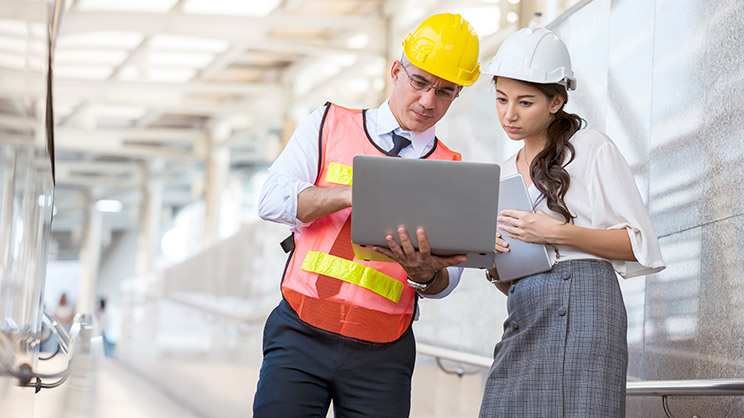 Two people discussing with laptop at construction site