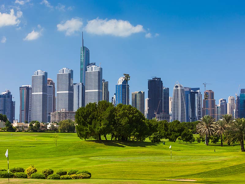 A lush golf course set against a backdrop of towering buildings, illustrating the contrast between greenery and urban life.