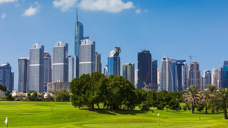 A lush golf course set against a backdrop of towering buildings, illustrating the contrast between greenery and urban life.