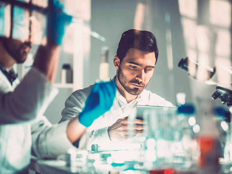 Two men wearing lab coats studying a tablet together, demonstrating collaboration in a scientific environment.